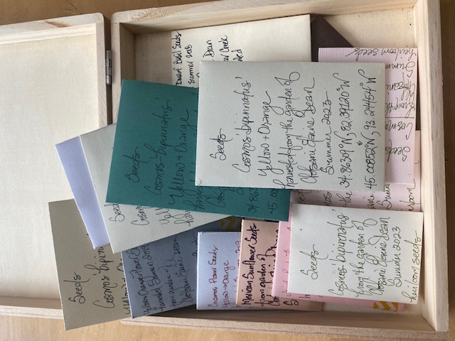 Box containing small paper envelopes, handwriting describes what seeds are contained