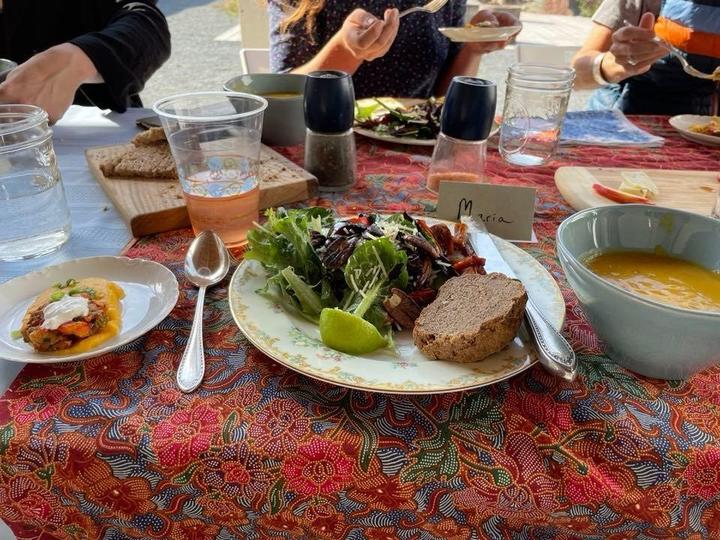 An attractive place setting with a green salad, flax seed bread, lemonade tinged pink by sumac, and yellow squash soup.