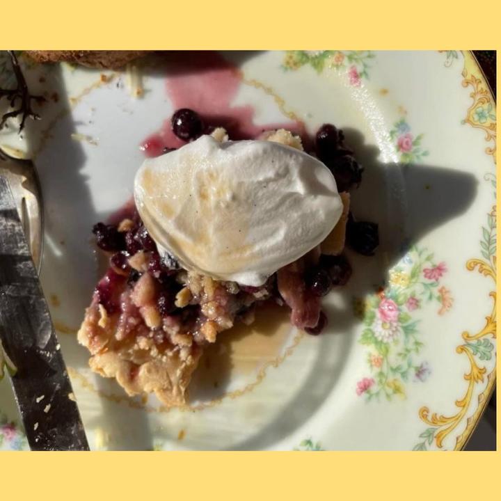 A slice of pie with dark berries, a crumbly crust and whipped cream on a white china plate