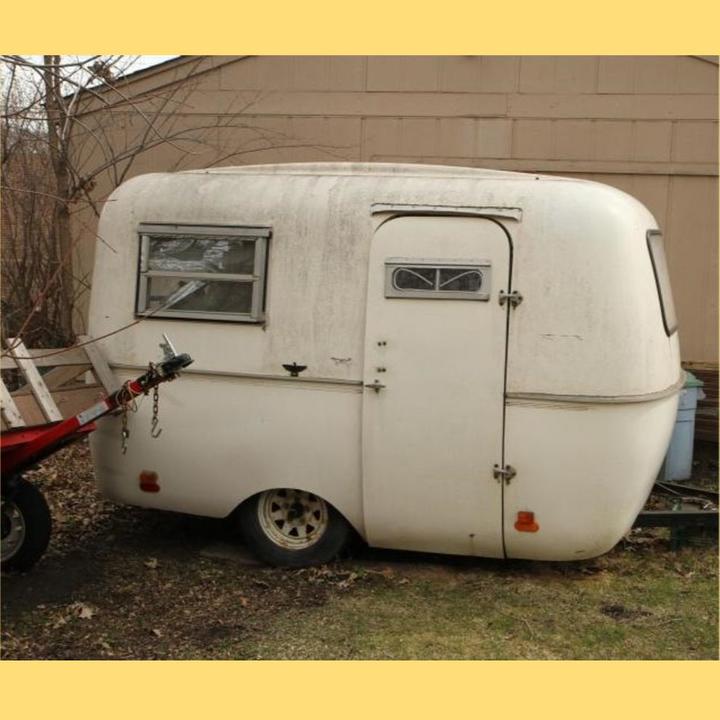 A streamlined mobile trailer looks unused, parked by a garage